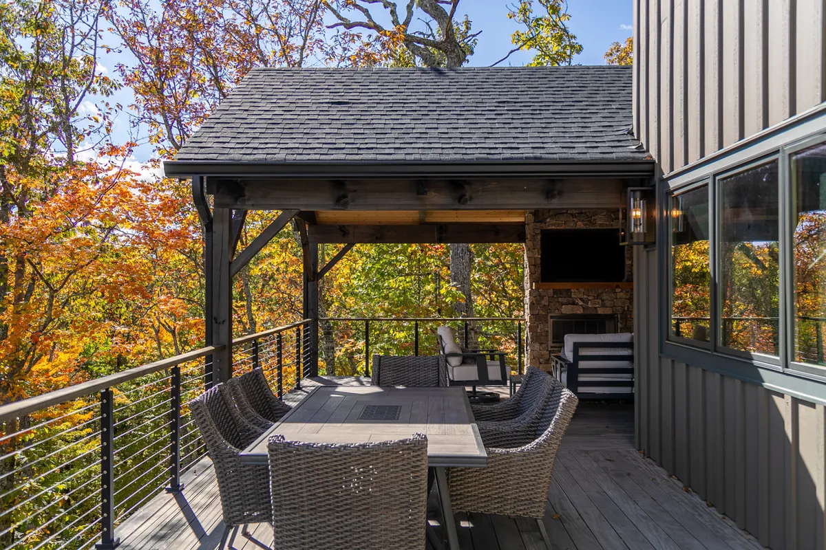 An inviting outdoor dining area is nestled among trees with a stone wall and comfortable seating. The space is set for lively gatherings and sunset meals, perfect for barbecue evenings or watching summer concerts in the fresh mountain air.