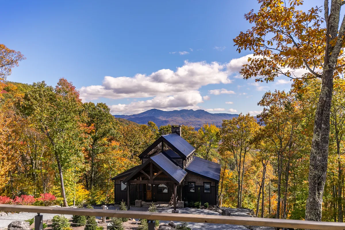 A modern cabin sits nestled amid colorful autumn foliage, with expansive mountain views beyond. The photo speaks to the allure of the Blue Ridge landscape, suggesting opportunities for hiking, exploring, and seasonal festivities.