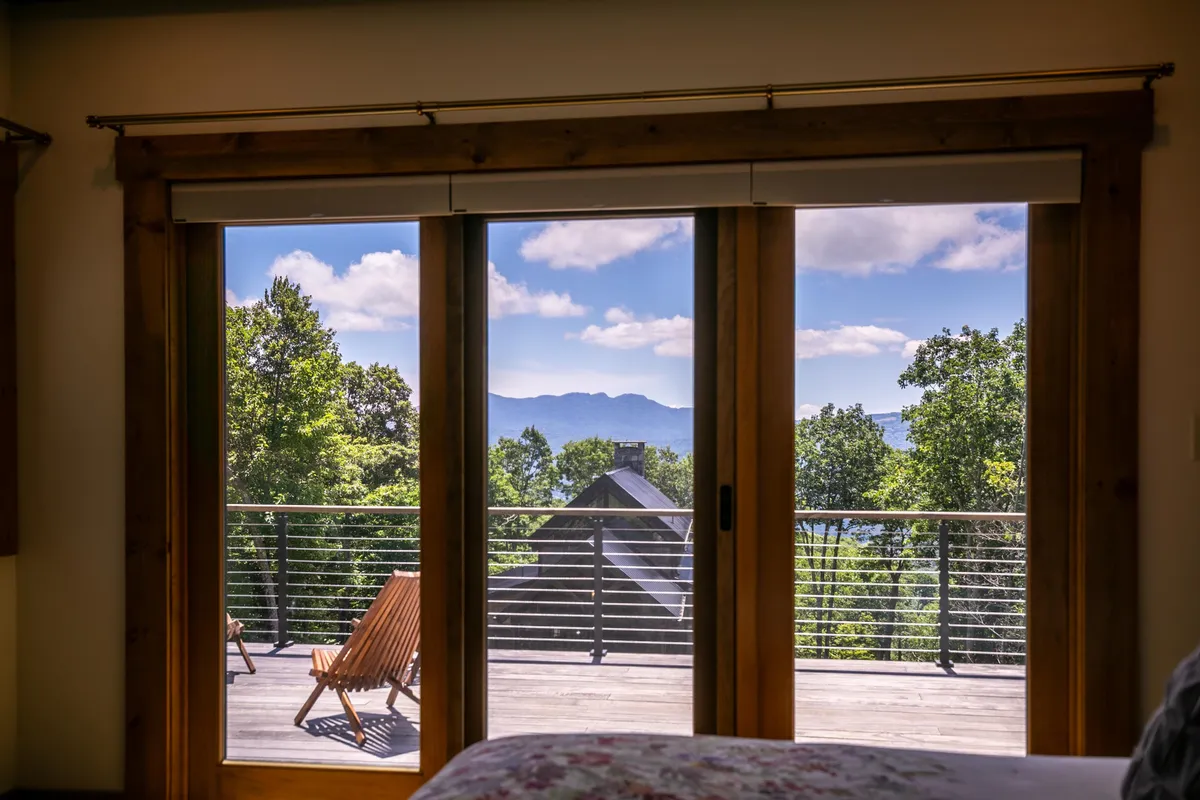 Sunlight pours through large glass doors that open to a wraparound deck, offering unobstructed mountain views. Comfortable outdoor chairs invite guests to step outside and enjoy the beauty, further blending the line between indoor and outdoor living.