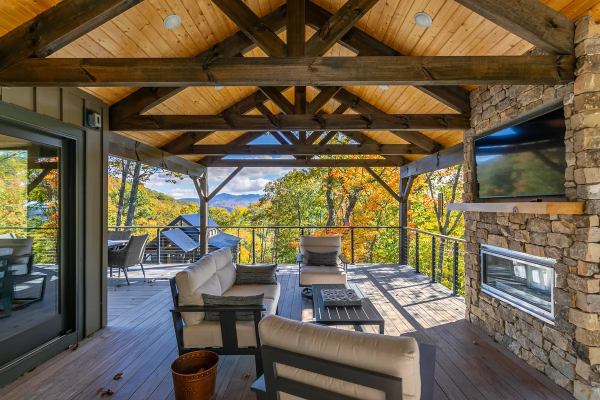 This image shows an inviting exterior gathering space with wooden beams, a stone fireplace, comfortable seating, and a stunning mountain view beyond. The area is arranged for outdoor dining and socializing, capturing the ambiance of relaxed, fireside evenings and group connection in the fresh mountain air.