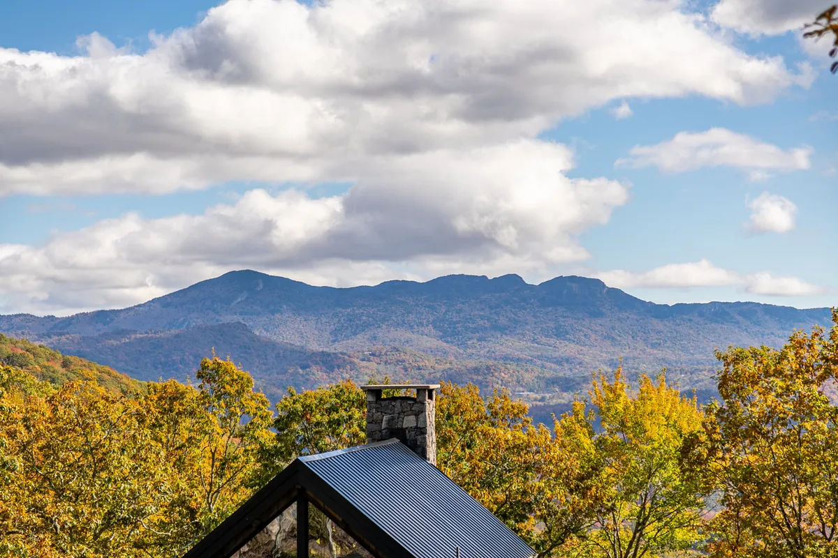 A serene view of the mountain range framed by colorful trees and a stone chimney, suggesting tranquility, the allure of the outdoors, and opportunities for hiking or simply absorbing nature's inspiration.