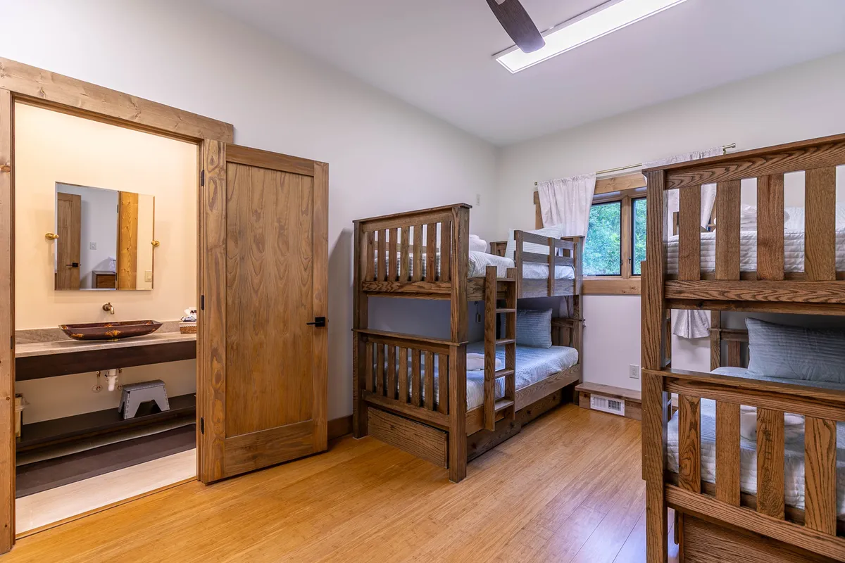 A playful, welcoming bunk room featuring sturdy wooden bunk beds, a built-in sink area, and a rustic wooden door. The setup is ideal for family stays, offering both functionality and comfort for children or groups.