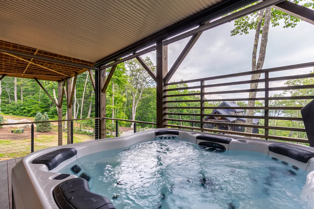 An exterior view of the lodge’s lower deck, featuring a generously sized hot tub surrounded by nature. The setting is peaceful and secluded, with the hot tub inviting guests to relax while soaking in the scenic views and fresh mountain air.