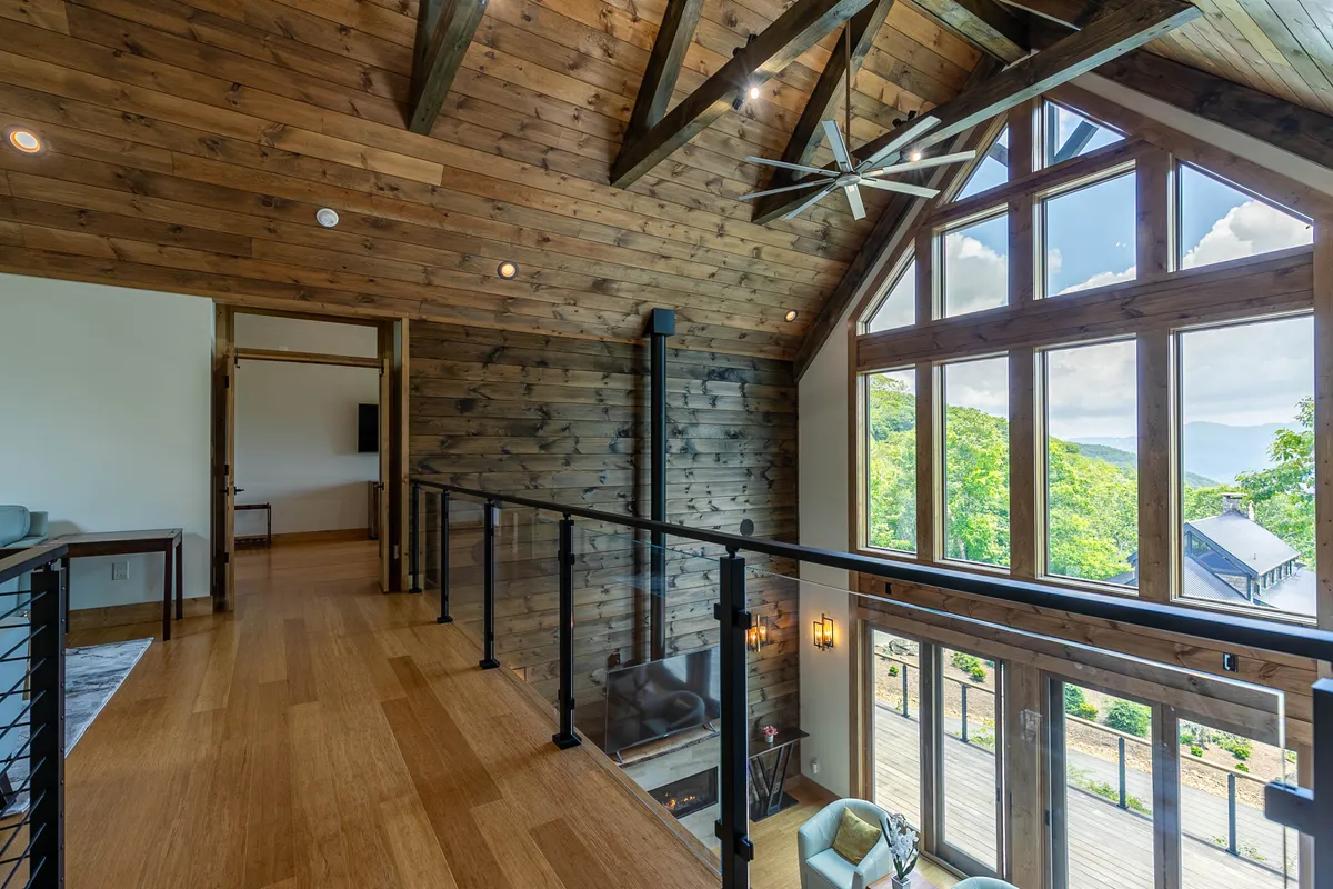 A cozy interior living area with large windows that frame stunning natural vistas, exposed wooden ceiling beams, and contemporary furnishings. The space is arranged for both intimate gatherings and larger celebrations, with the inviting fireplace as a central feature.