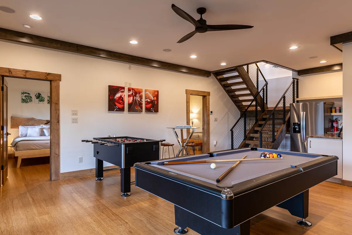 A lively recreation room equipped with both a pool table and a foosball table, set against a backdrop of a staircase and tasteful wall art. The room exudes a playful energy, ideal for group gatherings and spirited game nights.