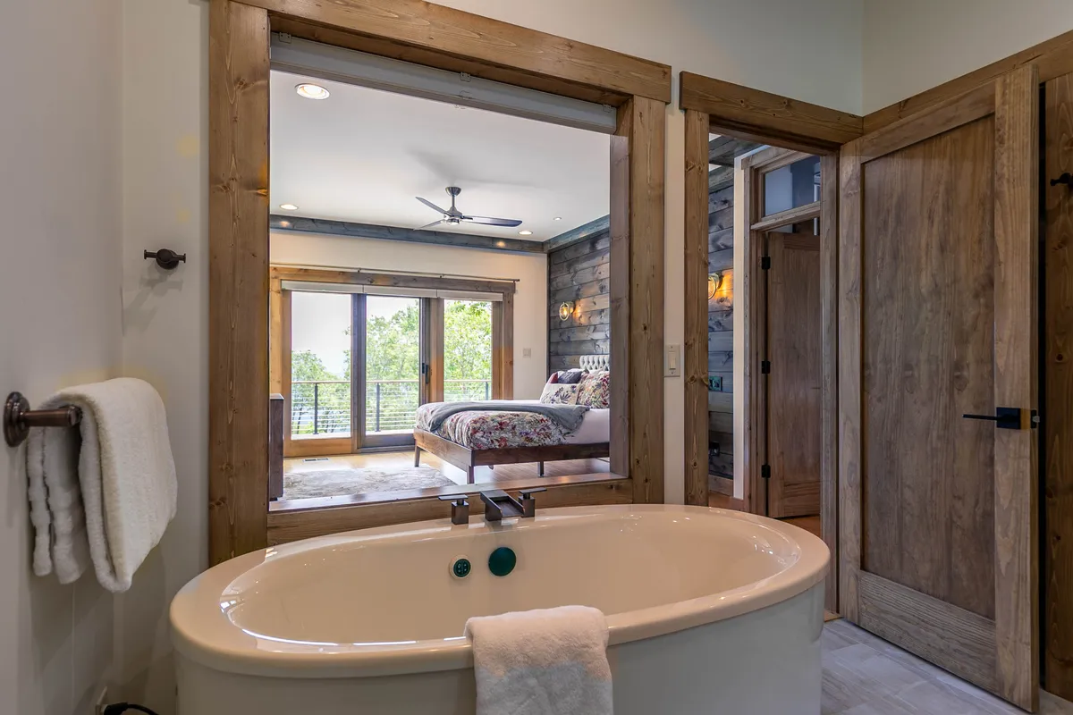 A tranquil bedroom featuring a plush bed with floral bedding, elegant wooden doors, and a freestanding bathtub positioned to enjoy scenic mountain views. The space is softly lit and exudes a spa-like atmosphere for relaxation and rejuvenation.