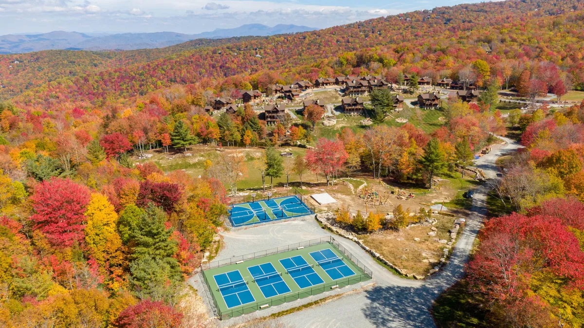 This image features colorful autumn foliage, tennis courts, and distant mountain views, set against a backdrop of residential buildings. The scene captures energetic outdoor activities and the vibrant, natural environment surrounding the lodge, ideal for team-building and sports.