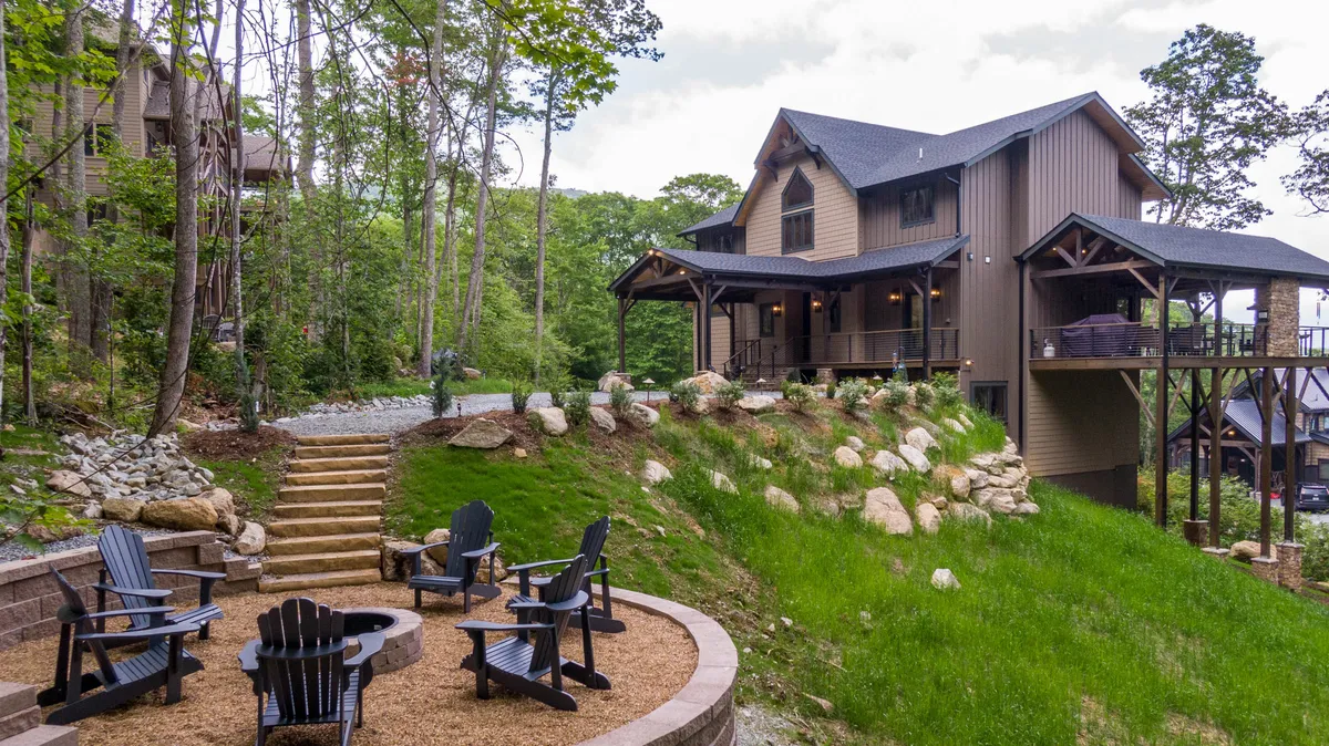 The hero image showcases the exterior of a luxurious mountain home with beautifully manicured landscaping, inviting outdoor seating, and a crackling fire pit, all set against the scenic backdrop of Banner Elk. The space is designed for guests to gather with family and friends, whether enjoying cozy fireside evenings or relaxing mornings surrounded by nature.
